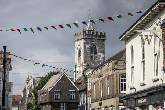 Salisbury, United Kingdom - 23 July 2026: View of Salisbury Cathedral tower rising above historic buildings and streets decorated with colorful bunting under a cloudy sky.