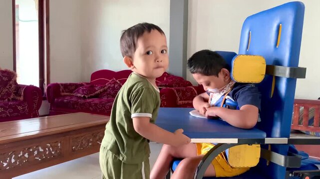 Young child interacting with a peer seated in a specialized ergonomic chair in a home setting, video clip