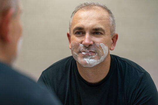 Man shaving with razor using foam in bathroom in the morning