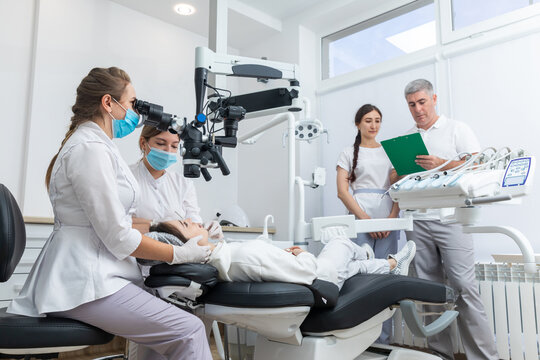 Group of young doctors learning in dental clinic watching dental treatment with microscope