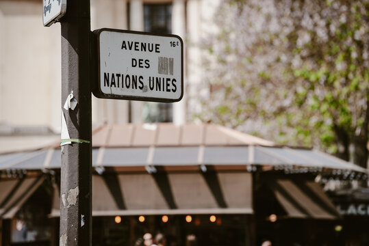 Paris, France - 06 May 2022: View of the street sign for Avenue des Nations Unies in Paris, France, with a blurred kiosk and trees in the background.