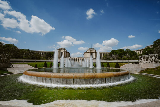 Paris, France - 06 May 2022: View of the Trocadero fountains with the Palais de Chaillot in the background under a bright blue sky with scattered clouds.