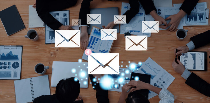 Aerial view of a business meeting with teams engaged in discussion, surrounded by charts and email icons, showcasing digital communication and strategic planning. Trope