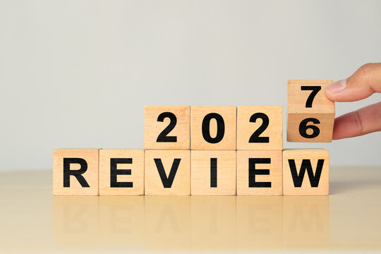 Hand flips wooden cube from 2026 to 2027 over REVIEW word, showing end of year summary and future planning