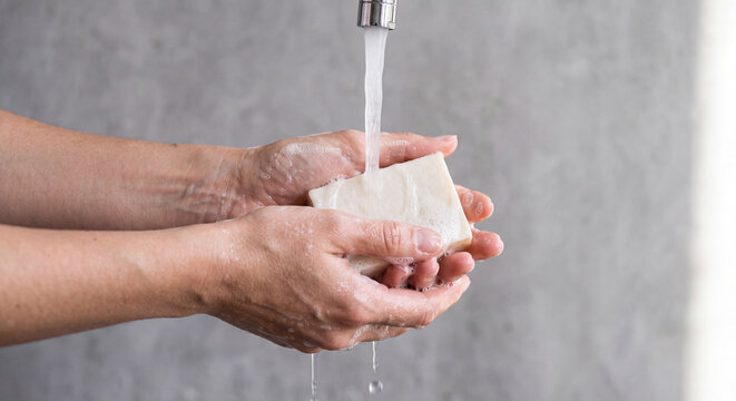 Close up shot of hands washing with organic bar soap under clean running tap water.