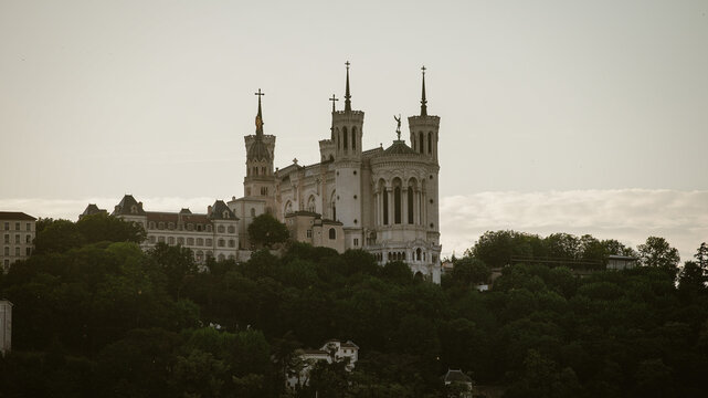 Lyon, France - 10 May 2022: View of Basilique Notre-Dame de Fourviere perched on Fourviere hill, surrounded by lush green trees under a soft overcast sky.