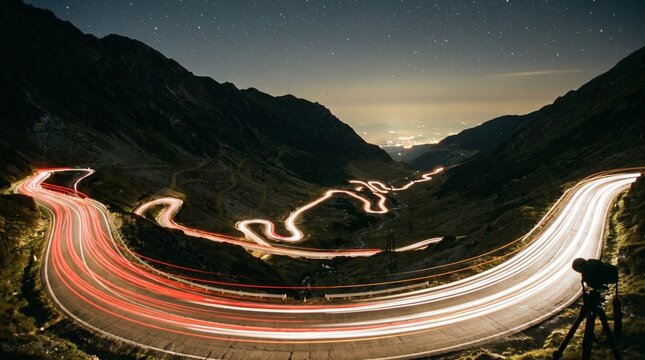 Long exposure photograph of car light trails on a winding mountain road at night, showcasing dynamic movement.