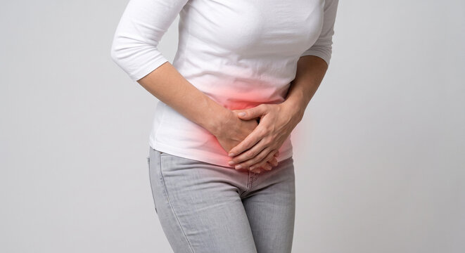 holding lower abdomen suffering from severe pelvic pain, cystitis, or menstrual cramps with red glowing area indicating inflammation