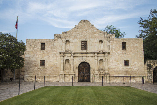 San Antonio, United States - 17 May 2013: View of The Alamo mission with its historic limestone facade, arched wooden entrance, and manicured lawn under a clear blue sky.