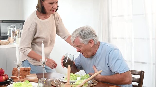 Elderly man choking at dining table while companion offers help and watches, clutching chest appearing distressed in sudden emergency, caregiver concern reflex response with salad and drink