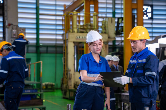 Team of industrial worker is checking the setup value of  metal casting machine by automated monitor while working inside roof factory for safety industry
