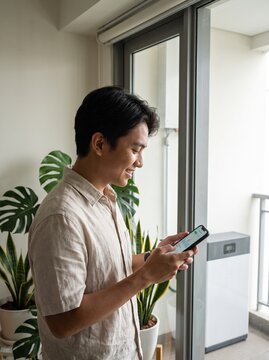 Man Using Mobile Phone by Window with Plants