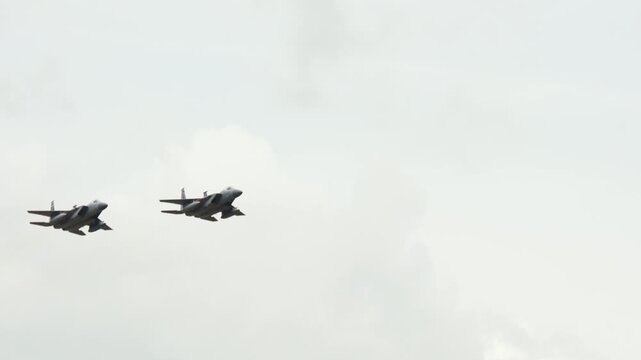Two military fighter jets fly together across an overcast sky.