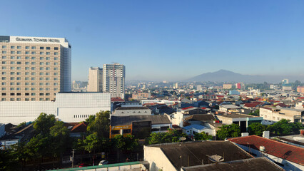 Naklejka premium Semarang, Indonesia - August 14, 2026: Panoramic city view of Semarang, Indonesia featuring high-rise buildings and Mount Ungaran under a clear blue sky