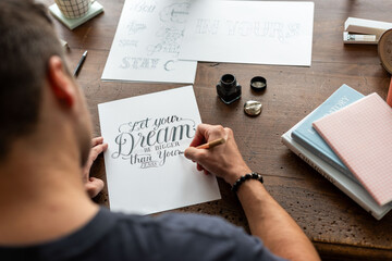 Obraz premium Person practicing calligraphy at a wooden desk with ink and paper.
