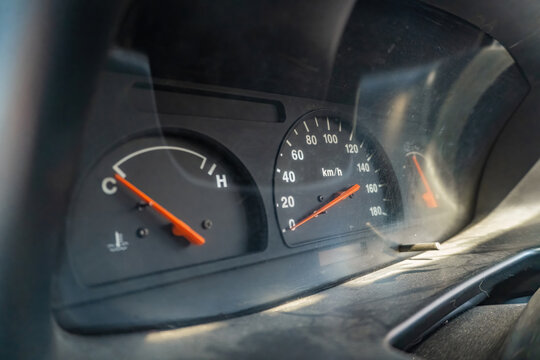 Detailed close up view of a car dashboard instrument cluster featuring an analog speedometer and temperature gauge during daytime.