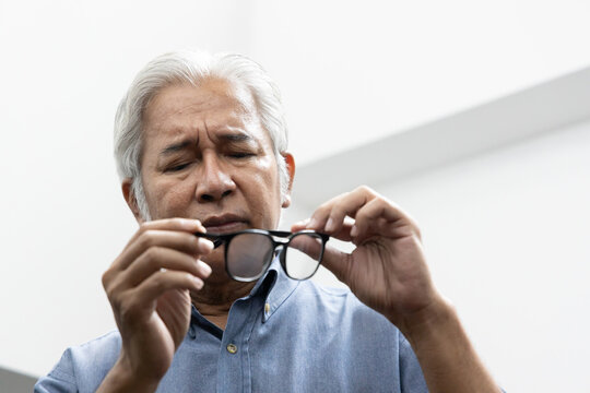 Sad Asian old senior man with eyesight problem, concept image of aging eye sight, vision deterioration, eyesight impair, optical problem with his eyeglasses, eye care, front view dutch angle