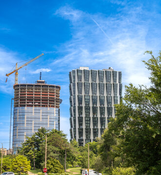 St. Louis, Missouri, United States - 07 August 2026: View of modern high-rise buildings, one under construction with a yellow crane, set against a blue sky and lush green trees.