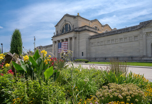 St. Louis, Missouri, United States - 07 August 2026: View of the Saint Louis Art Museum with an American flag, vibrant flower beds, and lush greenery under a blue sky.