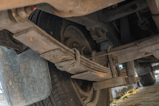 Close up undercarriage view of a rusty car leaf spring suspension system and wheel, highlighting classic vehicle maintenance, heavy-duty suspension repair, and automotive care.
