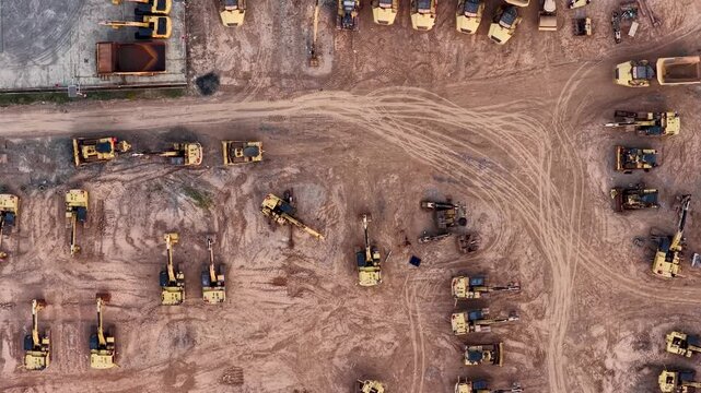 Aerial view showing rows of yellow excavators and heavy machinery parked on dirt ground
