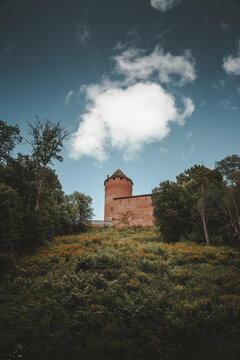 Sigulda, Latvia - 25 July 2023: View of Turaida Castle, a medieval red brick fortress, rising above a lush green hillside under a bright blue sky with scattered clouds.