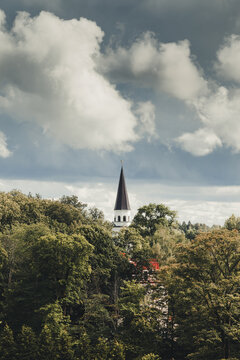 Sigulda, Latvia - 25 July 2023: View of the church spire rising above the dense green forest under a dramatic cloudy sky in Sigulda.
