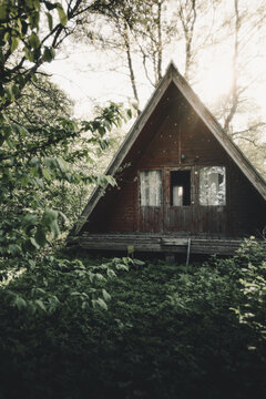 Merikula, Harju maakond, Estonia - 19 May 2023: View of a rustic A-frame wooden cabin nestled in a lush forest with sunlight filtering through the surrounding trees.