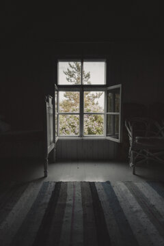 Laane County, Estonia - 08 June 2023: View of an open window looking out at blooming lilacs from a rustic room with a striped rug and wooden furniture on Vormsi island.