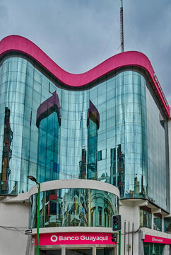 Ambato, Ecuador - October 28, 2025: Modern Banco Guayaquil building with reflective glass facade and pink roof, pedestrians walking on the street in an urban setting