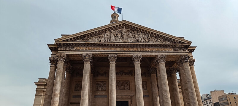 Paris, France - 04 April 2026: View of the Pantheon, featuring its neoclassical facade, Corinthian columns, detailed pediment sculpture, and the French flag flying atop the dome.