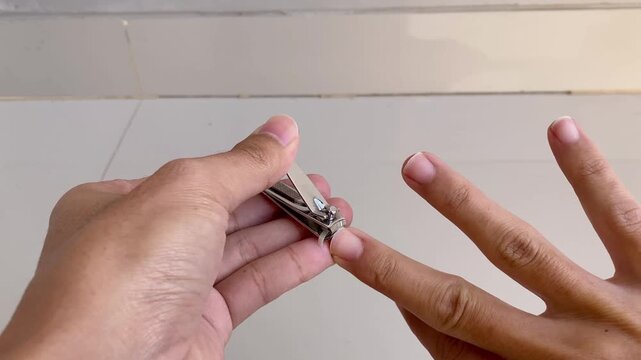 A close up view of a person using a metal nail clipper to trim their fingernails for personal grooming and hygiene.
