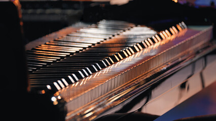 Closeup of piano keys illuminated by warm stage lights, shallow depth of field creates soft bokeh background. Polished black surface reflects golden glow © VeNN