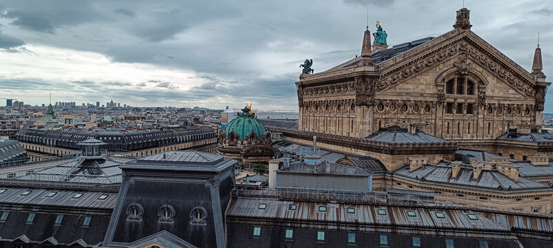 Paris, France - 03 April 2026: View of the Palais Garnier with its ornate roof and copper dome rising above the historic Parisian cityscape under a cloudy sky.