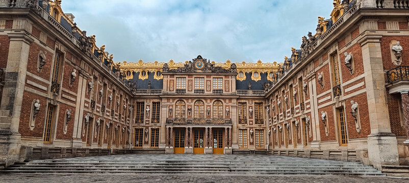 Paris, Ile-de-France, France - 02 April 2026: View of the ornate facade of the Palace of Versailles with its signature red brick and stone architecture and golden roof details.