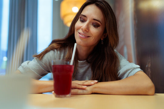Happy Woman Smiling While Drinking Fresh Red Juice With Straw. Smiling elegant woman enjoys refreshing red beverage sitting inside cozy modern restaurant setting