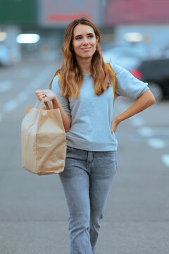 Confident Female Customer Holding Paper Grocery Bag Standing In Parking Lot. Smiling young woman carries paper shopping bag near supermarket outdoors in car park