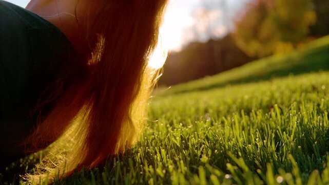 CLOSE UP, LENS FLARE, DOF: Young woman lies down on green grassy slope with her eyes closed in golden autumn light of sunset. Relaxation and quiet enjoyment while exploring the hills in countryside.