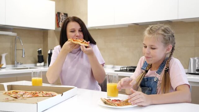 Happy Smiling family of two eagerly eat delicious pizza, little girl daughter with sits with her mother at the table eating italian pizza, looking at each other smiling