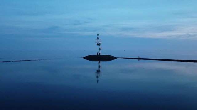 Navigation beacon in the Wadden Sea near West-Terschelling, Terschelling, Friesland, Netherlands, revealing a stone breakwater, calm tidal waters and blue hour reflections, drone push-in.