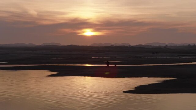 People relaxing on tidal flats in the Wadden Sea near Terschelling, Friesland, Netherlands, revealing winding tidal creeks, sandbanks, coastal dunes and golden sunset reflections drone pullback