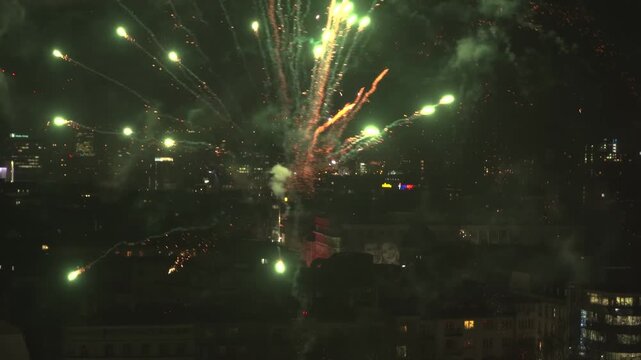 Wide night view of fireworks over central Sofia, Bulgaria, filmed from an elevated viewpoint, with city lights, skyline, smoke trails and festive bursts in the sky.