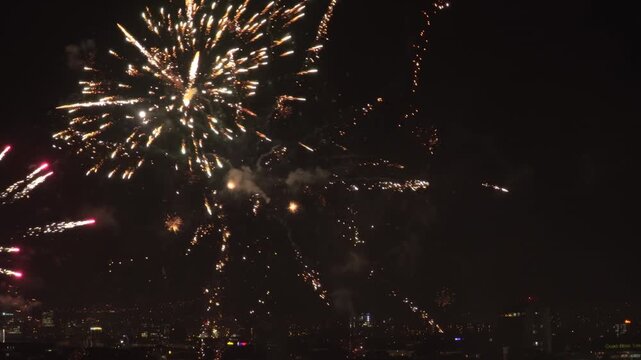Close night view of bright fireworks bursting over Sofia, Bulgaria, with sparkling trails, smoke clouds and city lights below the dramatic night sky.