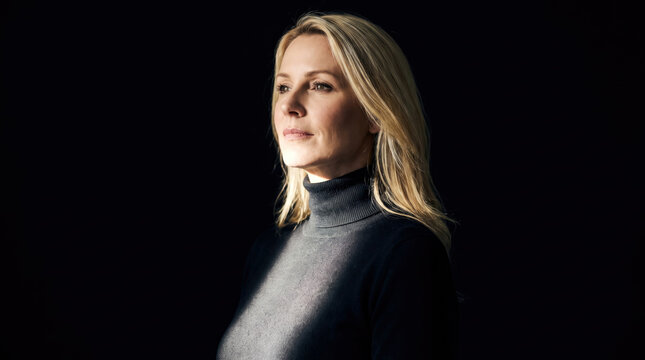 Portrait of a blonde woman wearing a black turtleneck sweater against a dark studio background