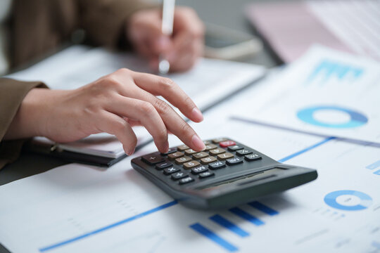 Businesswoman using a calculator to analyze financial reports with charts and graphs, representing accounting, budgeting, expense calculation, data analysis, business planning, and finance management.