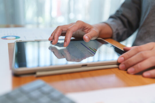 Close-up of hands using a touchscreen tablet to review financial dashboards, analyze business data, and support planning in a modern digital workspace.