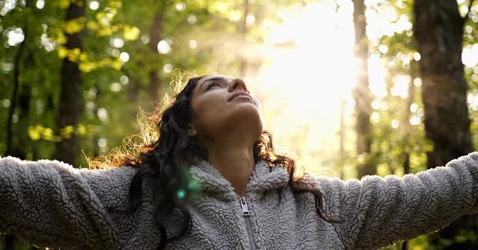 Woman with arms outstretched enjoying sunlight in a forest.