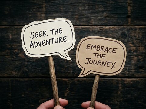 A human hand gently holds two speech bubbles displaying inspirational quotes seek the adventure and embrace the journey against a rich dark wooden
