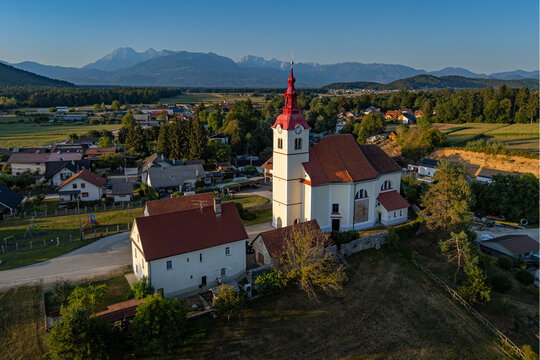 Elevated view of the Church of St. Lucy (Cerkev sv. Lucije) and the rural village of Skaručna with the Kamnik-Savinja Alps in the background, Vodice, Slovenia