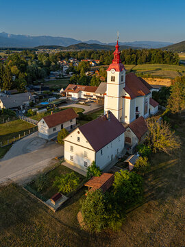 Vertical aerial view of the Baroque Church of St. Lucy (Cerkev sv. Lucije) in Skaručna illuminated by late afternoon golden hour sunlight, Vodice, Slovenia
